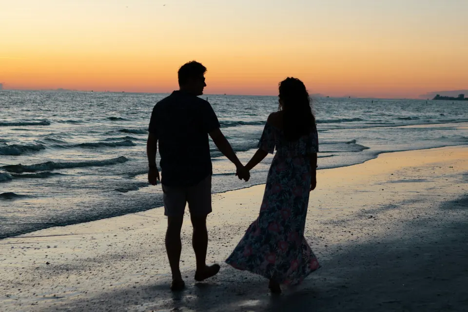 A couple walking hand in hand along the beach at sunset